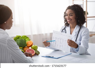 Smiling African Doctor Dietologist Showing Patient Black Woman Treatment Plan During Consultation In Clinic