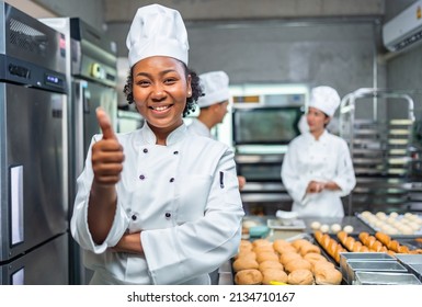 Smiling african  female bakers looking at camera..Chefs  baker in a chef dress and hat, cooking together in kitchen.Team of professional cooks in uniform preparing meals for a restaurant in  kitchen. - Powered by Shutterstock