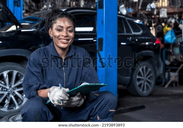 Smiling African female car mechanic holding\
customer chart working in auto repair service shop,black woman\
mechanic checking car problem lists in vehicle garage , automobile\
repair service concept