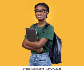 Smiling African Female Student Holding Laptop Hugging Computer Posing Standing On Yellow Studio Background. E-Learning And Educational Gadgets, Distant Online Study And Student's Lifestyle Concept