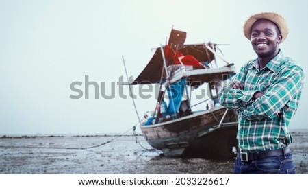 A smiling African fisher man stands beside his fishing boat