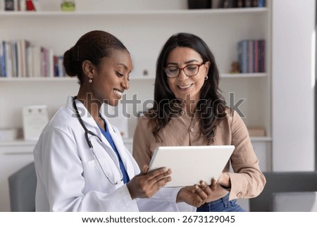 Smiling African general practitioner using tablet, showing to 60s woman patient diagnostics result, treatment plan or procedure, give recommendation, share good health news during her visit in clinic