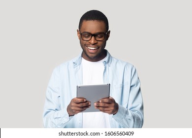 Smiling african guy hold tablet digital device having fun using application browsing sites, shopping in internet, flirting with girlfriend via online dating websites isolated on gray studio background