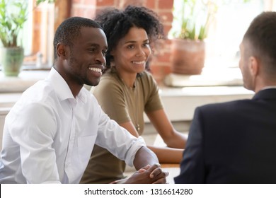 Smiling African Hr Managers Recruiters Listening To Male Applicant At Recruiting Job Interview, Happy Black Couple Consulting Realtor Insurer Bank Worker Making Offer To Clients At Meeting In Office