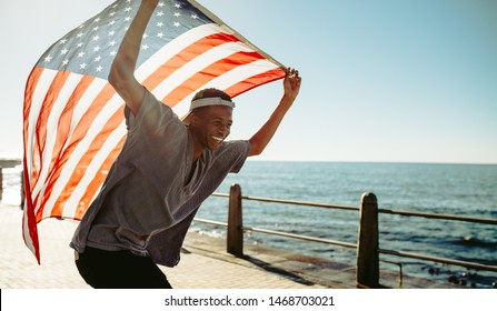 Smiling african man on seaside promenade with an american flag. Cheerful young guy at promenade holding american flag. - Powered by Shutterstock