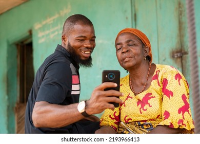 smiling african man shows an old african woman content on his phone - Shutterstock ID 2193966413