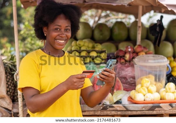 smiling african market lady using her phone and\
credit card