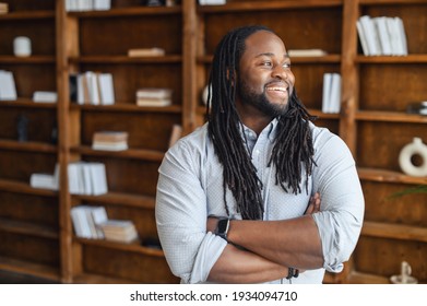 Smiling African office employee with dreadlocks in smart casual wear stands with arms crossed in contemporary coworking office space, a multiracial guy looks away and laughs. Diverse work team concept