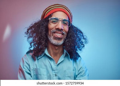 Smiling African Rastafarian Male Wearing A Blue Shirt And Beanie. Studio Portrait On A Blue Background.