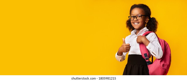 Smiling African Schoolgirl Gesturing Thumbs-Up Approving School Standing On Yellow Studio Background. Panorama, Empty Space For Text