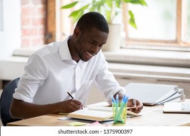 Smiling African Student Do Easy Exercise Homework Assignment Preparing For Test Sitting At Desk Feels Satisfied, Hold Pen Makes Notes Reading Textbook Chapter, Interesting Study Self Education Concept