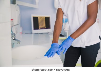 Smiling African Woman Dentist Cleaning Up Dentist Chair After Procedures