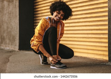 Smiling african woman in fitness wear tying her shoelace. Fitness woman tightening her shoes during workout.