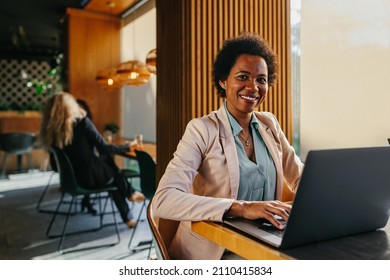 Smiling African Woman Sits At Cafe Table, Looking At Laptop Screen, Watching Educational Video, Working Remotely On Computer In Coffeeshop. Remote Work