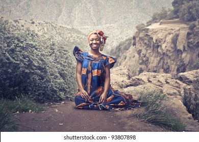 Smiling African Woman In Traditional Clothes Sitting On A Rock