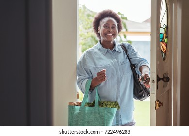 Smiling African Woman Walking Through The Front Door Of Her Home With A Shopping Bag Full Of Fresh Produce