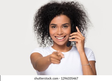 Smiling African Woman Wearing Wireless Headset With Microphone Looking Pointing Finger At Camera You Isolated On White Background, Black Call Center Customer Service Operator Or Telemarketer Portrait