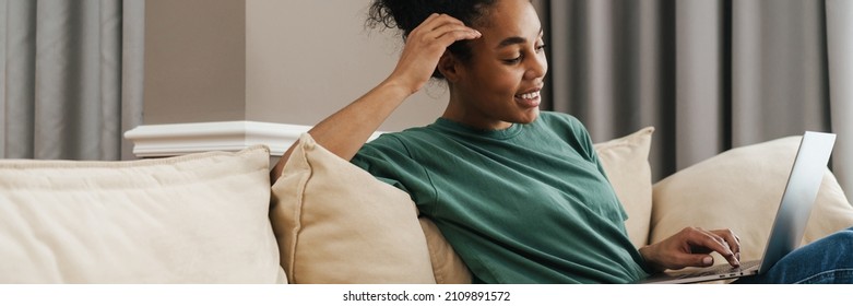 Smiling African Woman Working With Laptop At Home, Sitting On A Couch With Dog