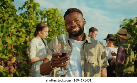 Smiling african young man holding wineglass toasting having a good time on wine tasting degustation holiday with friends. Vineyard. - Powered by Shutterstock