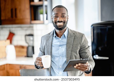 Smiling African-American businessman holding a coffee mug and tablet in a modern kitchen, ready to start his workday with a positive attitude. - Powered by Shutterstock