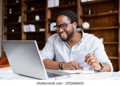 Smiling African-American guy takes notes watching webinars on the laptop,researching business tasks, a male student is studying online, listening video lectures, writes down, e-learning concept - Powered by Shutterstock