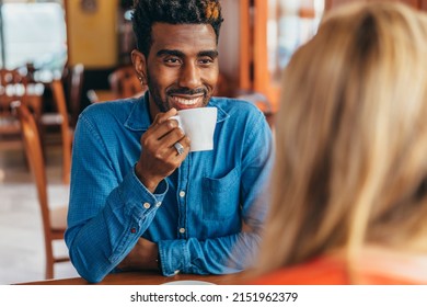 smiling African-American man sipping coffee while conversing with a blonde Caucasian woman - Powered by Shutterstock