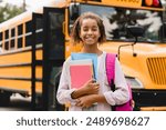 Smiling african-american schoolgirl going back to school with books and copybooks waiting for schoolbus. New academic year semester