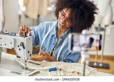 Smiling African-American seamstress adjusts sewing machine shooting new video in studio - Powered by Shutterstock