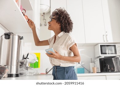 Smiling Afro American Lady Holding Mobile Phone While Going To Make Coffee On Office Kitchen