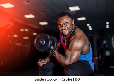 Smiling afro american sports man looking at camera over black background with dumbbell in hand. Perfect muscular body with strong muscles.