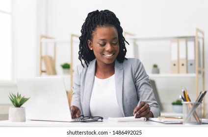 Smiling Afro Businesswoman Working On Laptop And Taking Notes In Modern Office. Free Space - Shutterstock ID 1486492025
