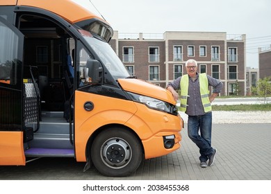 Smiling aged Caucasian bus driver in eyeglasses and green vest leaning on bonnet while waiting for passengers - Powered by Shutterstock