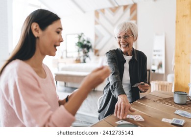 Smiling aged diverse best friends laughing while gathering at table playing board game drinking hot beverages enjoying spending time together - Powered by Shutterstock