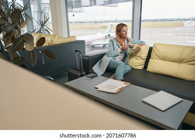 Smiling airline passenger drinking coffee in airport lounge - Shutterstock ID 2071607786