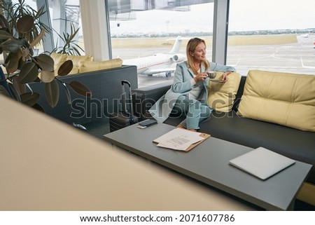 Smiling airline passenger drinking coffee in airport lounge