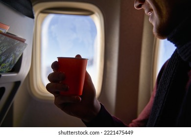 Smiling Airline Passenger With A Paper Cup Of Coffee Looking Ahead In Airplane Window. Man Drinks Tea Onboard. Male Holds Beverage Or Water During Flight.