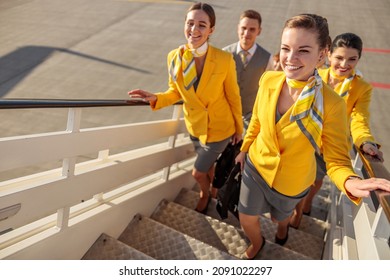 Smiling airline workers walking up airplane stairs