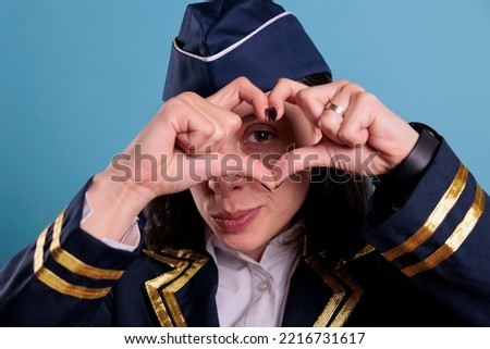 Smiling airliner stewardess showing heart shaped love symbol with fingers, conceptual romance gesture. Friendly air hostess in aviation uniform expressing affection feelings front view medium shot