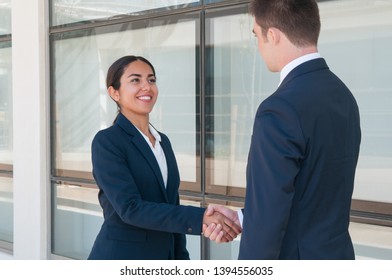 Smiling ambitious business woman saying good bye to partner. Young man and woman in formal suits shaking hands. Business handshake concept