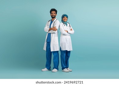 Smiling arab male and female doctors posing in uniform over blue background, full length studio shot of professional medical workers standing with folded arms, successful physicians looking at camera - Powered by Shutterstock