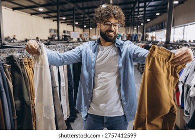 Smiling Arab man comparing different pants in a clothing store, enjoying the shopping experience and looking for new outfits