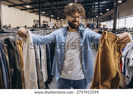 Smiling Arab man comparing different pants in a clothing store, enjoying the shopping experience and looking for new outfits