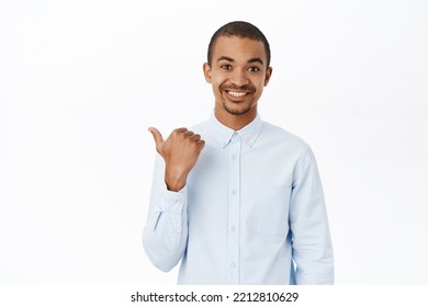 Smiling Arab Man Pointing Left, Showing Direction, Company Logo Or Banner Aside, Standing Over White Background In Blue Collar Shirt