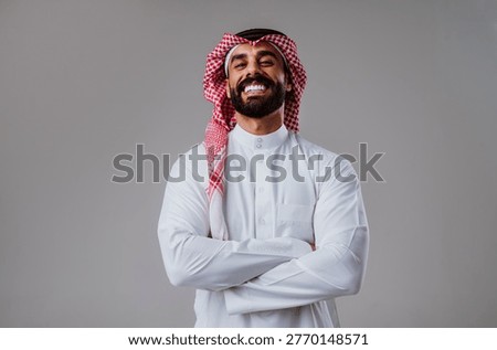 Smiling arab man posing confidently with arms crossed in traditional middle eastern clothing, representing cultural identity, success, and professional trust in a studio setting