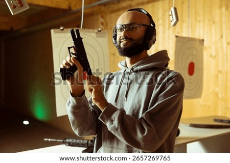 Smiling Arab shooting range client wearing protective glasses reloading gun following safety protocols. Happy Middle Eastern man loading pistol, handling weapon following methodical safety rules