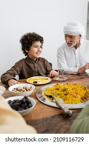 smiling arabian boy having family dinner near muslim grandfather