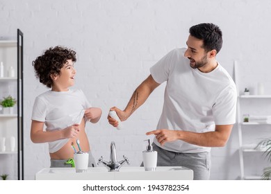 Smiling Arabian Man Holding Deodorant Near Son And Sink In Bathroom