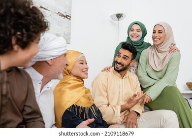 smiling arabian man pointing with hand while talking to cheerful multiethnic muslim family