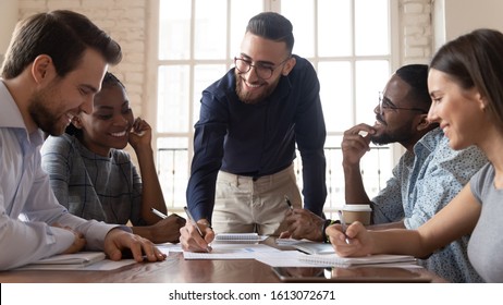 Smiling Arabian millennial businessman hold meeting with multiethnic colleagues explain financial paperwork at briefing, successful young Arabic male ceo or boss lead team briefing in office
