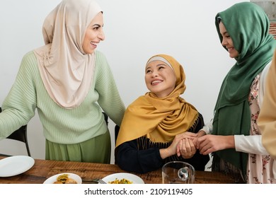 Smiling arabian woman looking at daughter and asian mom near food at home